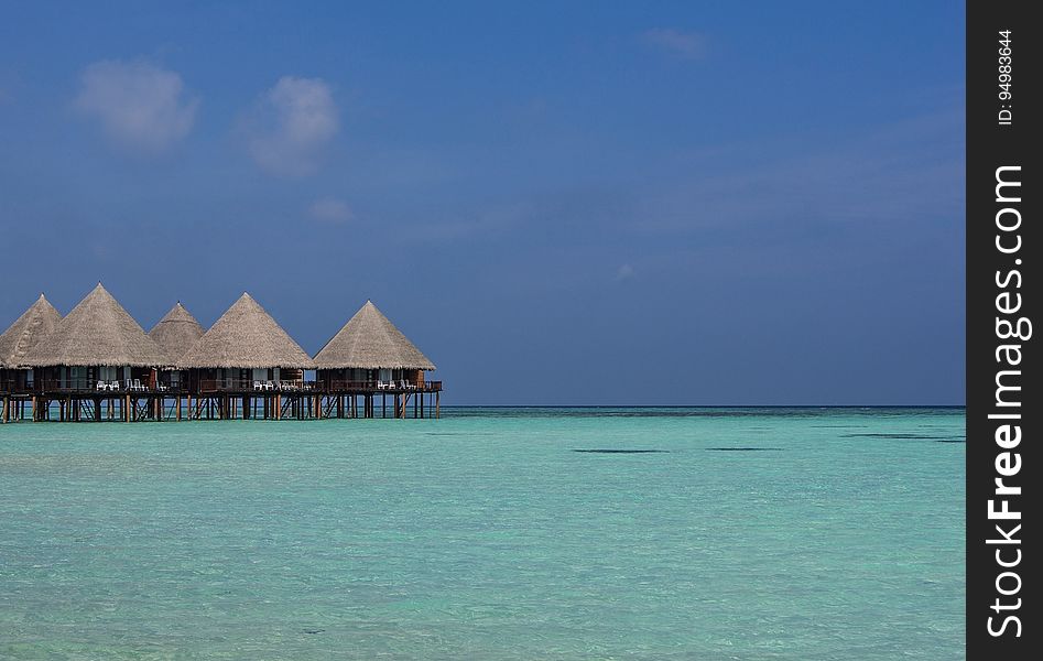 Resort bungalows in Maldives on wooden stilts over clear blue water against blue sunny skies. Resort bungalows in Maldives on wooden stilts over clear blue water against blue sunny skies.