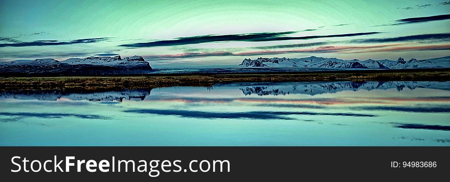 Panorama of mountains along coastline with green skies reflecting in calm waters. Panorama of mountains along coastline with green skies reflecting in calm waters.