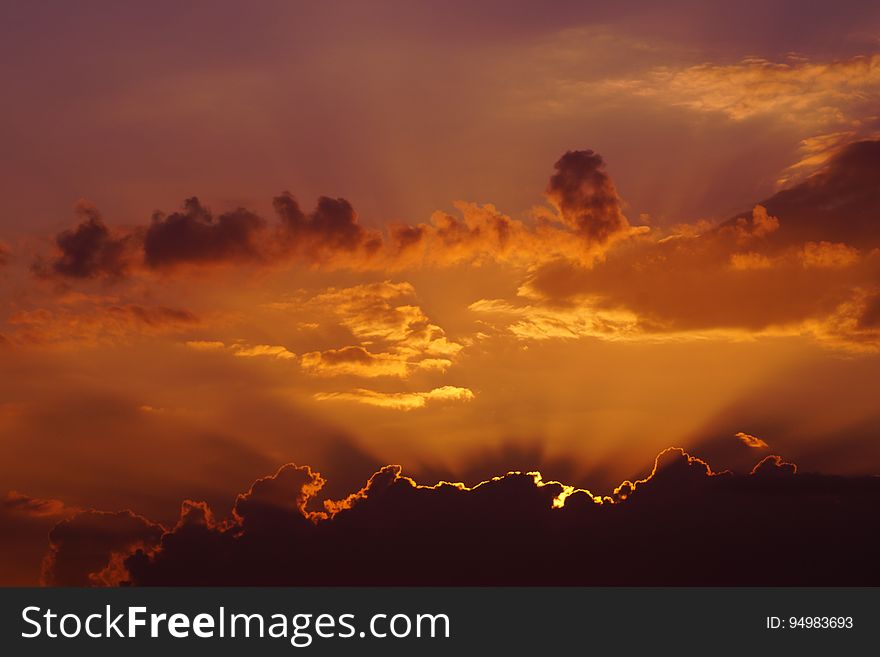 Orange skies at sunset behind clouds in sky.