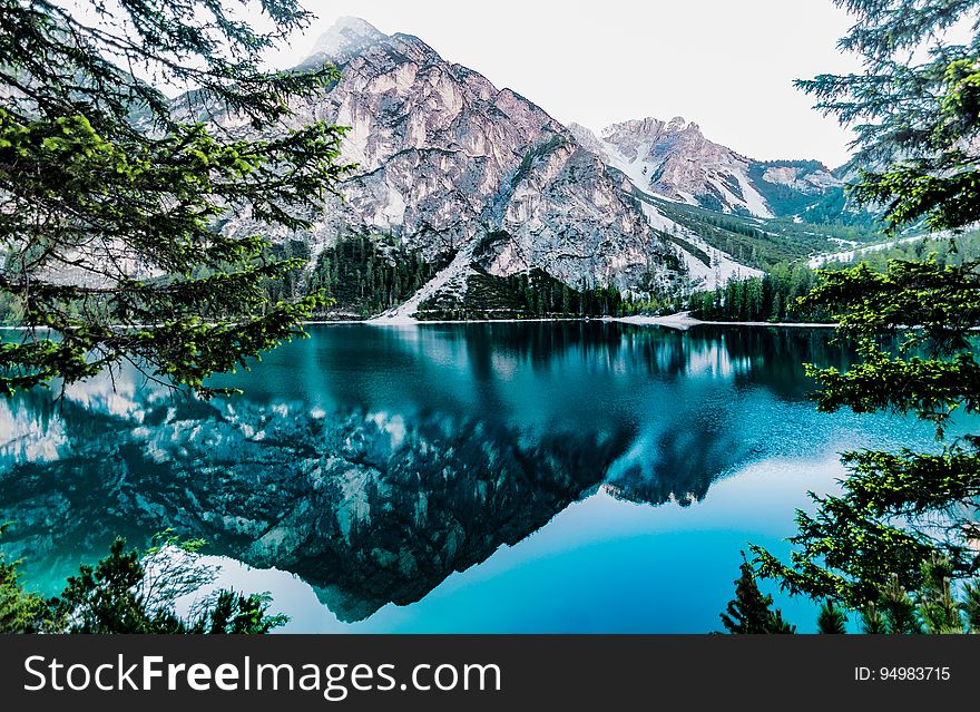 Mountain peaks reflecting in blue waters of alpine lake with green pine trees on sunny day. Mountain peaks reflecting in blue waters of alpine lake with green pine trees on sunny day.