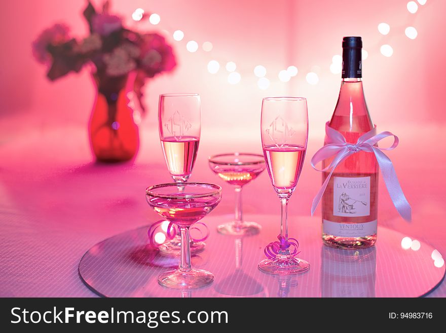 A bottle of rose wine or champagne with glasses on a table in red color. A bottle of rose wine or champagne with glasses on a table in red color.