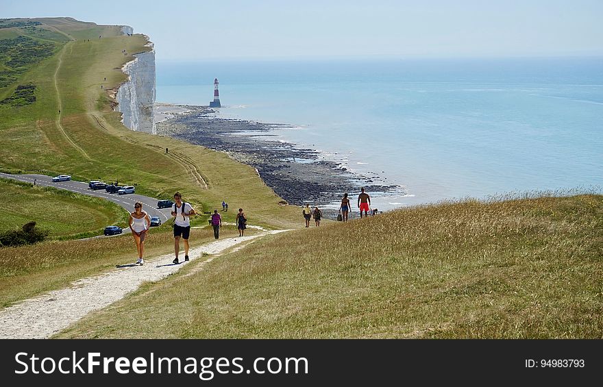 People walking at the White Cliffs of Dover at the Strait of Dover with a lighthouse in the distance.
