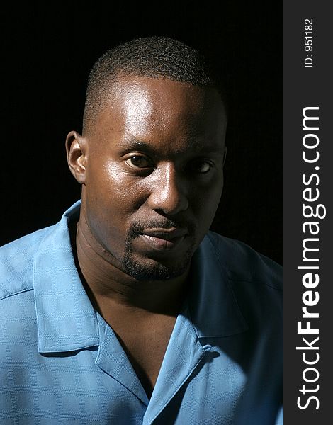 Low key portrait headshot on black background of a handsome African American male with a serious expression. Low key portrait headshot on black background of a handsome African American male with a serious expression.