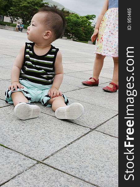 Cute Asian boy sitting on the ground - girl in the background