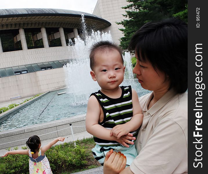 Korean woman holding her baby - young girl dancing in the background. Korean woman holding her baby - young girl dancing in the background