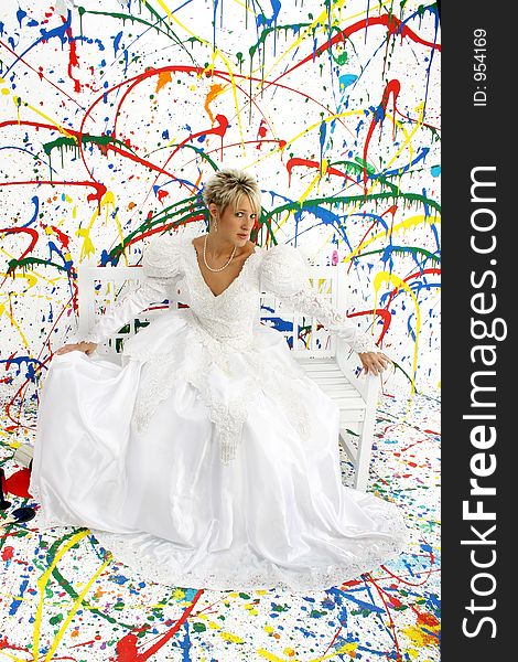 Beautiful young woman in bridal gown sitting on bench; splattered paint background. Beautiful young woman in bridal gown sitting on bench; splattered paint background