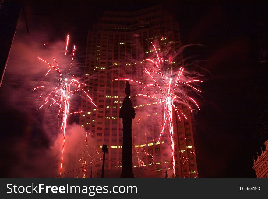 Fireworks bursts in a downtown setting are set off in front of a skyscraper with a veterans memorial in the foreground (silhouetted between fireworks. Fireworks bursts in a downtown setting are set off in front of a skyscraper with a veterans memorial in the foreground (silhouetted between fireworks.