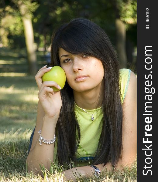 Beautiful girl lying on grass and holding green apple in hand. Beautiful girl lying on grass and holding green apple in hand