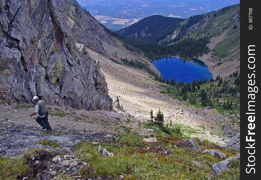 This is a picture of a hiker carefully picking his way down through the rugged and steep terrain toward the blue lake below. This is a picture of a hiker carefully picking his way down through the rugged and steep terrain toward the blue lake below.