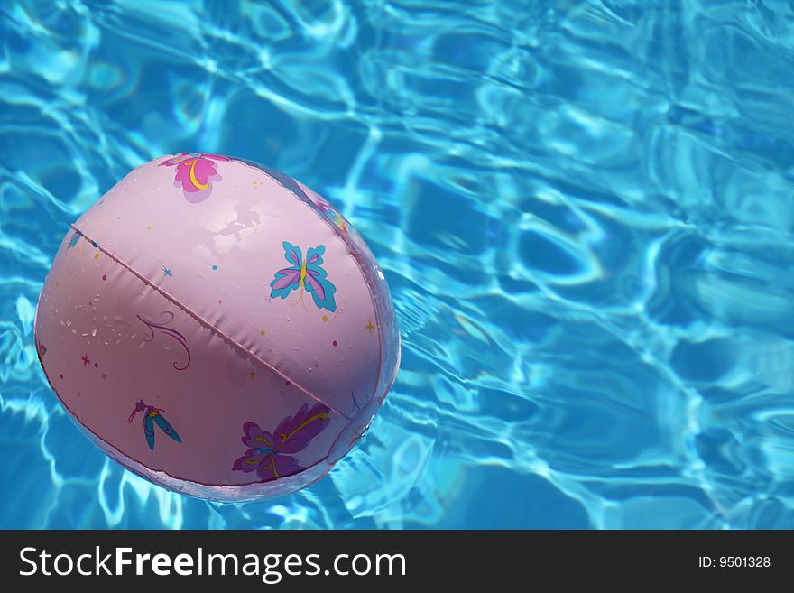 A plastic pink ball with butterflies floating on the surface of a swimming pool, focus is on the ball. A plastic pink ball with butterflies floating on the surface of a swimming pool, focus is on the ball