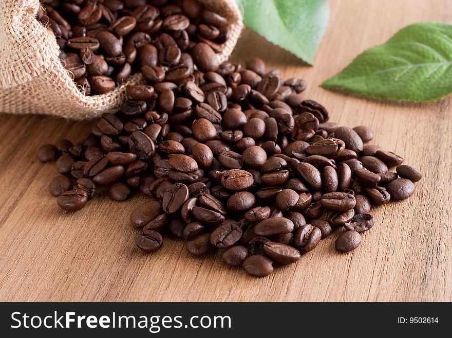 A bunch of coffee beans, falling out of a sack on a wooden background