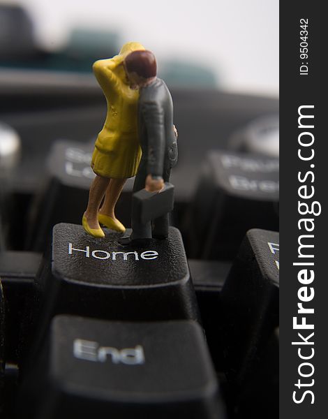 Miniature businessman and woman embracing on home button of keyboard. Miniature businessman and woman embracing on home button of keyboard