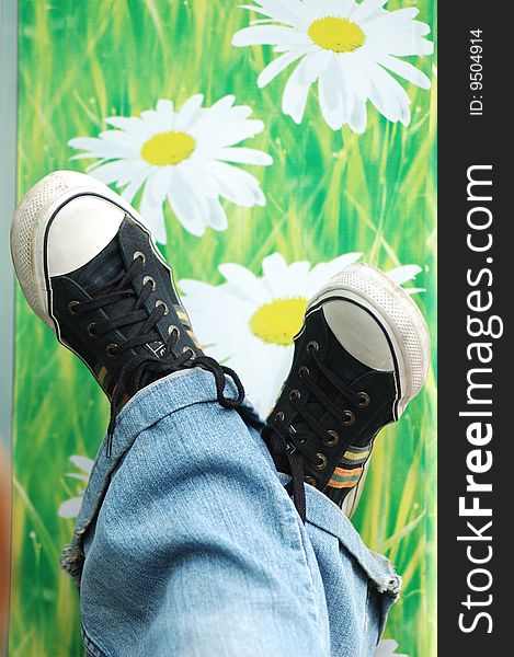 The legs, dressed in jeans and black canvas sneakers on the background pattern with daisies.