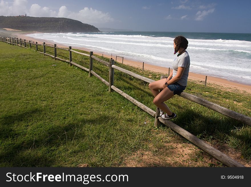 Young girl is siiting on the beach fence and watching the ocean. Young girl is siiting on the beach fence and watching the ocean.