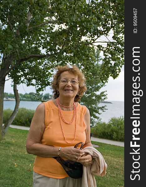 Smiling older lady walking outdoor by a lake. Smiling older lady walking outdoor by a lake