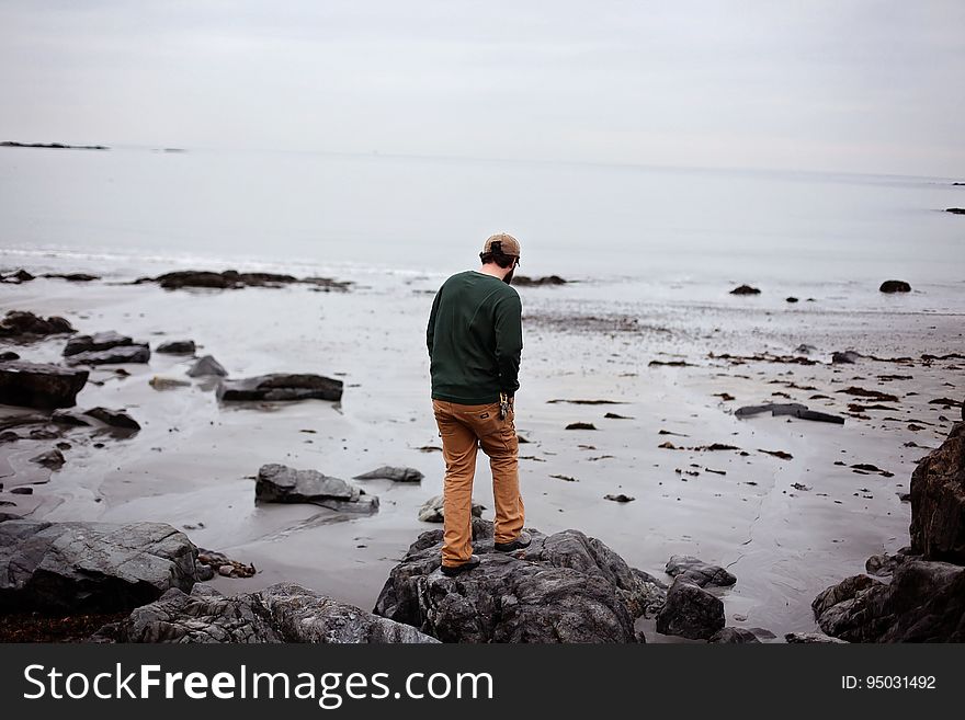 Man standing on large silvery gray rock on the shore at the seaside on a misty morning. Man standing on large silvery gray rock on the shore at the seaside on a misty morning.