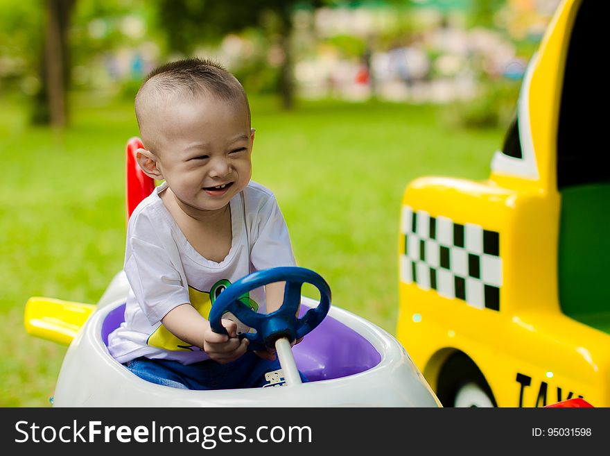 Happy smiling baby boy in white t-shirt driving toy car in the garden with yellow taxi alongside. Happy smiling baby boy in white t-shirt driving toy car in the garden with yellow taxi alongside.