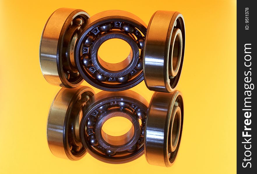 Three bearings are photographed with reflexion on a yellow background. Three bearings are photographed with reflexion on a yellow background