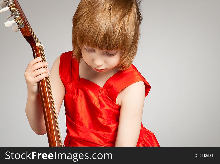 Girl in red dress play the guitar. On light-grey background. Girl in red dress play the guitar. On light-grey background.