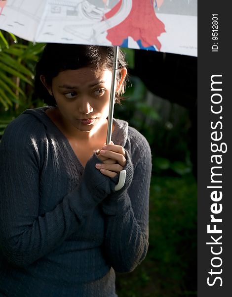 Beautiful asian woman holding an umbrella on a cold rainy day in the afternoon. looks worried to get wet. Beautiful asian woman holding an umbrella on a cold rainy day in the afternoon. looks worried to get wet.