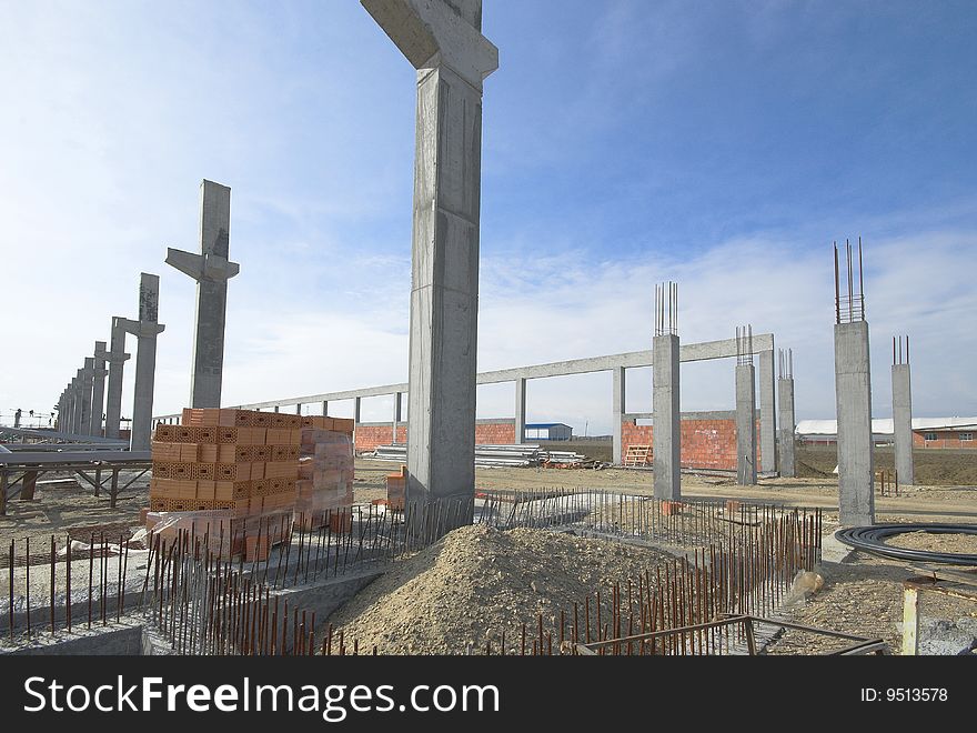 Reinforcement for concrete base in front and concrete columns in the background against the blue sky. Reinforcement for concrete base in front and concrete columns in the background against the blue sky