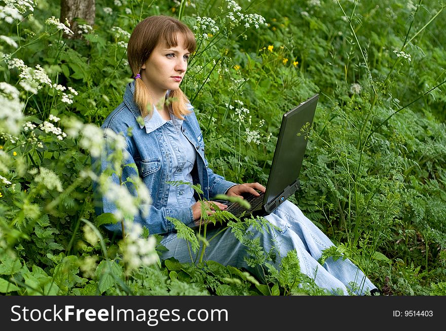 The beautiful girl with the laptop in park sits in a green grass. The beautiful girl with the laptop in park sits in a green grass