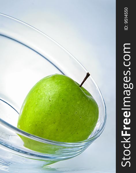 Green apple in glass plate on blue background