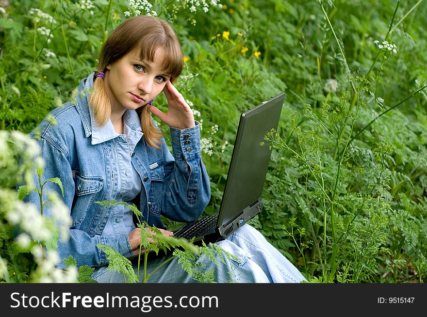 The beautiful girl with the laptop in park sits in a green grass. The beautiful girl with the laptop in park sits in a green grass