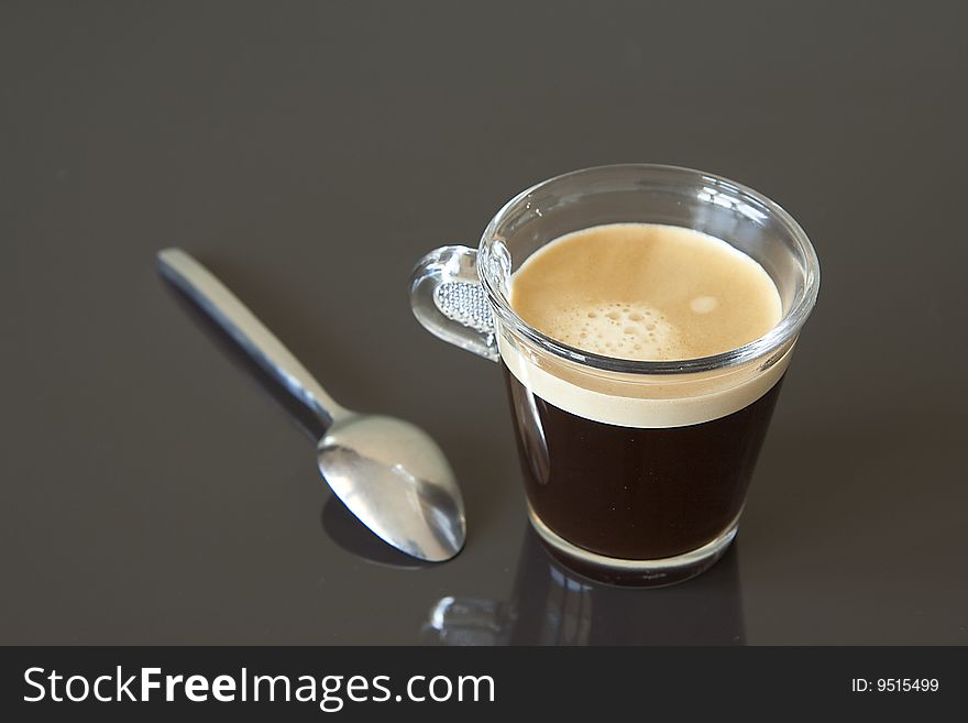 Strong black coffee in glass with spoon on the black background. Strong black coffee in glass with spoon on the black background