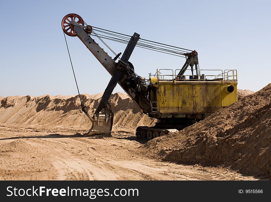 Rusty old yellow excavator on a sand