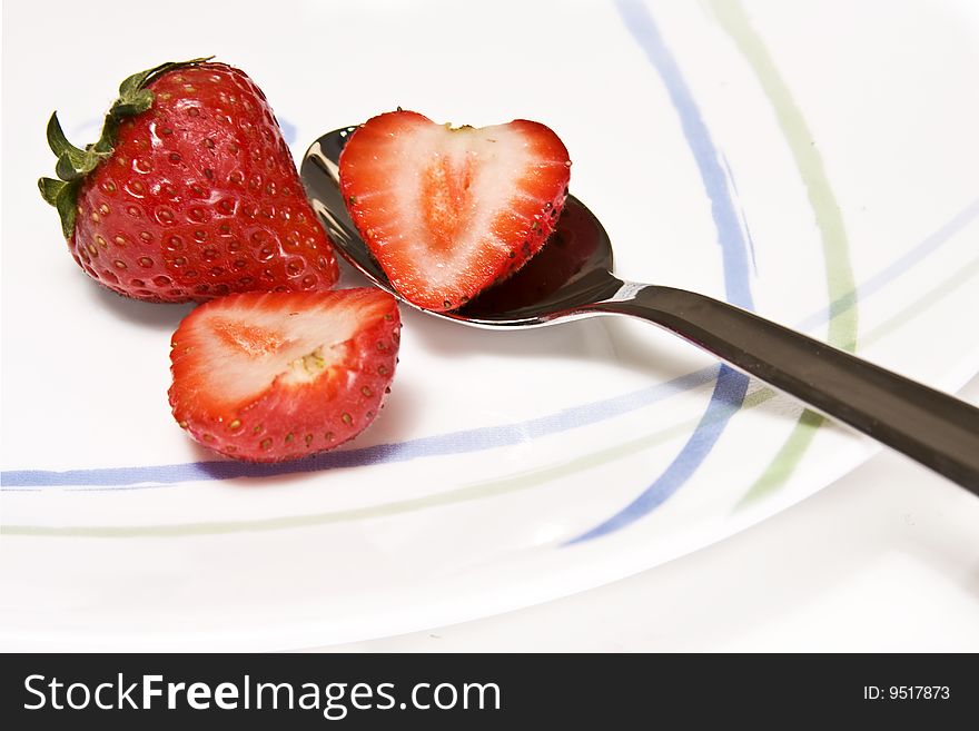 High key photo of a whole strawberry and two slices of strawberry set on a white plate. High key photo of a whole strawberry and two slices of strawberry set on a white plate