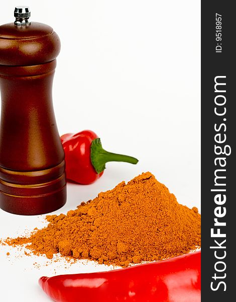 A composition of two pods of red chile pepper a wooden hand mill for grinding and a little of ground red pepper on a white background. A composition of two pods of red chile pepper a wooden hand mill for grinding and a little of ground red pepper on a white background