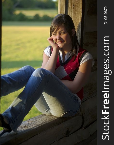 A teen girl sits in a cabin window lit by the warm glow of evening. A teen girl sits in a cabin window lit by the warm glow of evening.