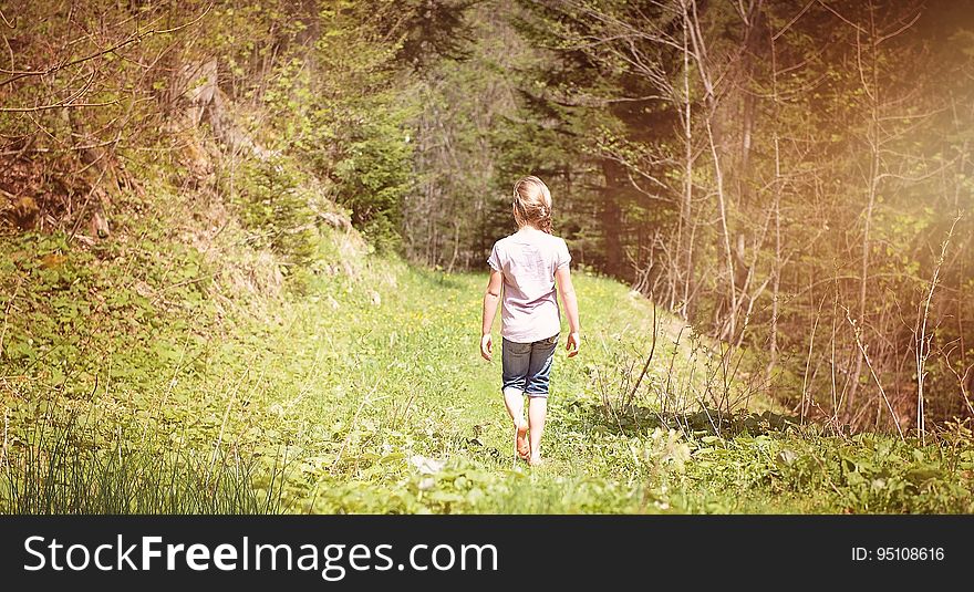 Young blond girl walking alone through a green landscape with grasses, ferns, bushes and trees. Young blond girl walking alone through a green landscape with grasses, ferns, bushes and trees.