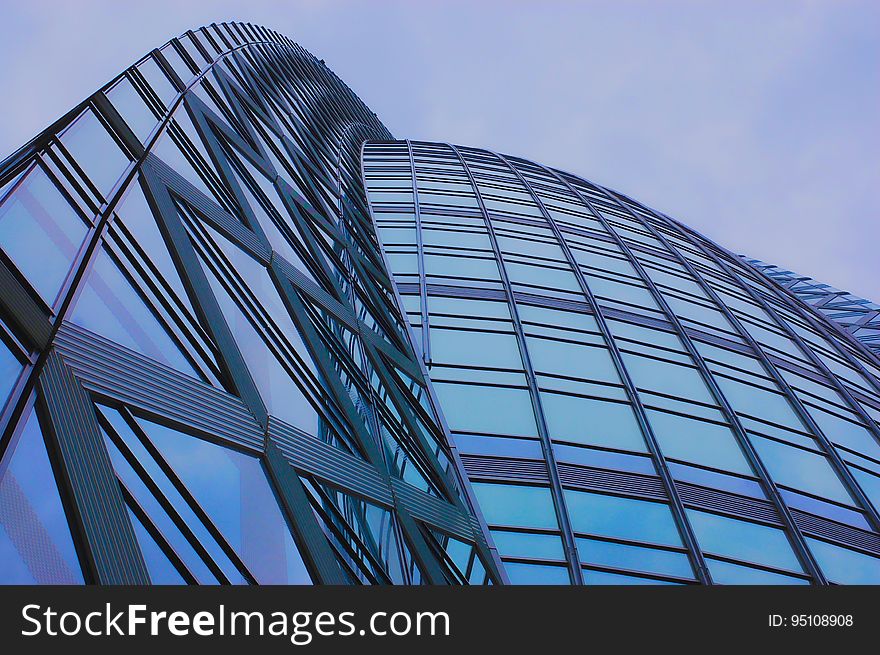 Curved architectural facade of high rise buildings constructed of glass, steel and concrete, pale blue sky reflected in the glass. Curved architectural facade of high rise buildings constructed of glass, steel and concrete, pale blue sky reflected in the glass.
