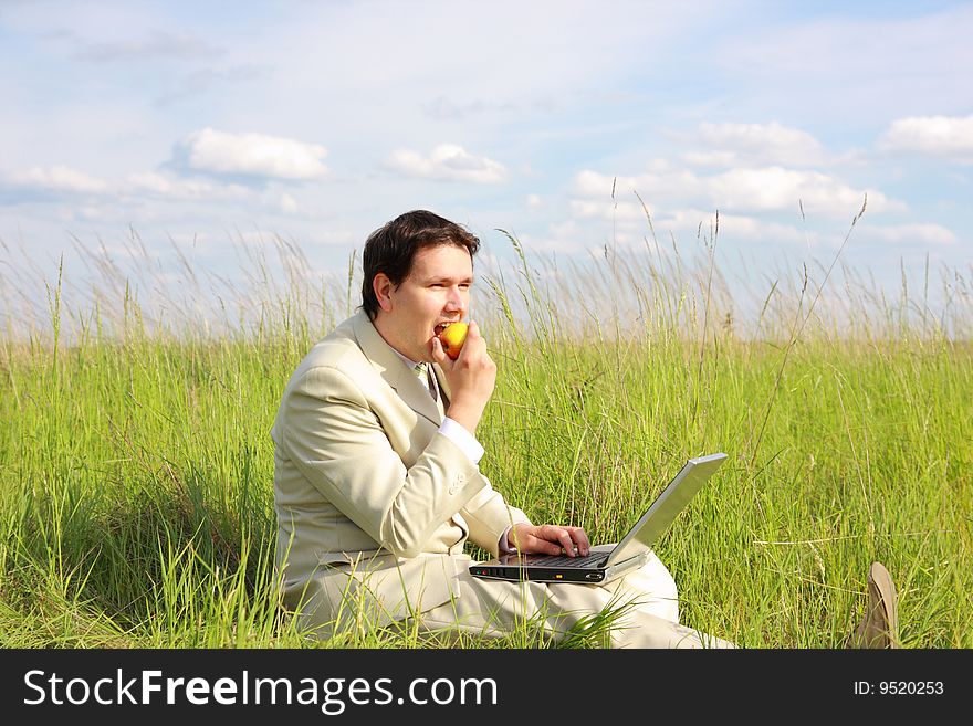 Businessman with laptop siting on green grass, eating apple, relaxing. Businessman with laptop siting on green grass, eating apple, relaxing