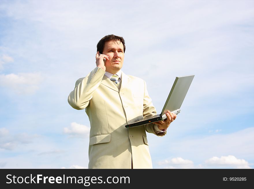 Businessman calling by the phone and holding laptop over blue sky with clouds. Businessman calling by the phone and holding laptop over blue sky with clouds