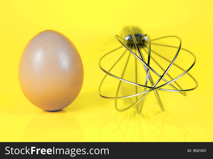 An egg and and a egg beater together isolated against a yellow background