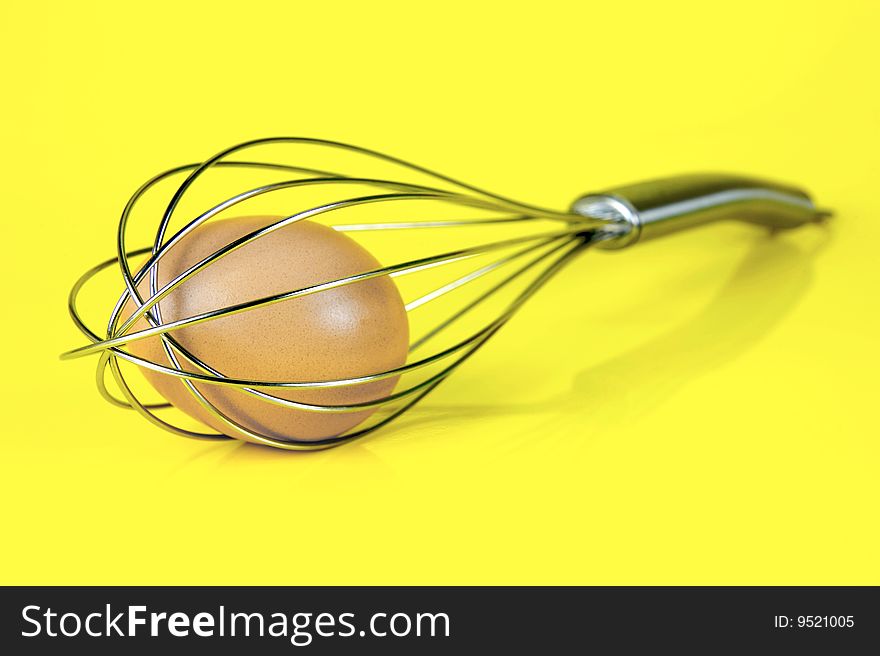 An egg and and a egg beater together isolated against a yellow background