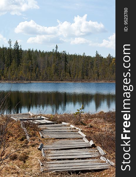 Old wooden pier to lake, coniferous wood, cloud