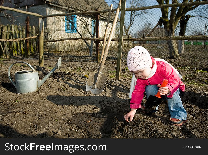 An anxious  little girl squatting down on the ground   cultivating soil with  a toy  spade. An anxious  little girl squatting down on the ground   cultivating soil with  a toy  spade