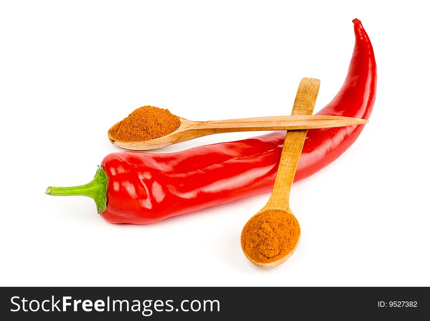 A pod of red hot chili and two wooden spoonful of ground red pepper across it on a white background. A pod of red hot chili and two wooden spoonful of ground red pepper across it on a white background