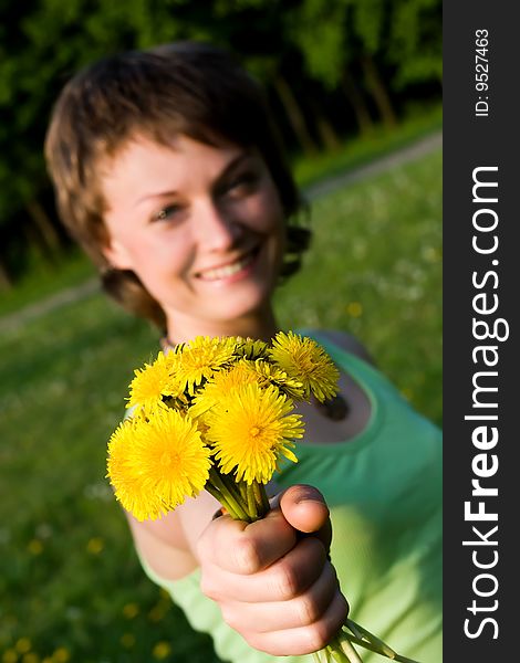 A young cheerful woman with a bunch of dandelions in her hand