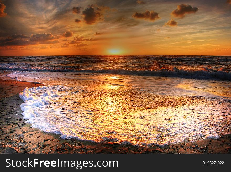 Beautiful golden sunset with incoming tide producing gold tinged white foam over a sandy beach. Beautiful golden sunset with incoming tide producing gold tinged white foam over a sandy beach.