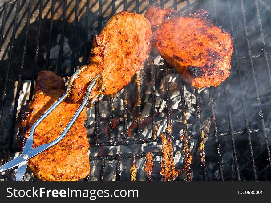 Pork shop being grilled and turned so it not will get burned. Pork shop being grilled and turned so it not will get burned