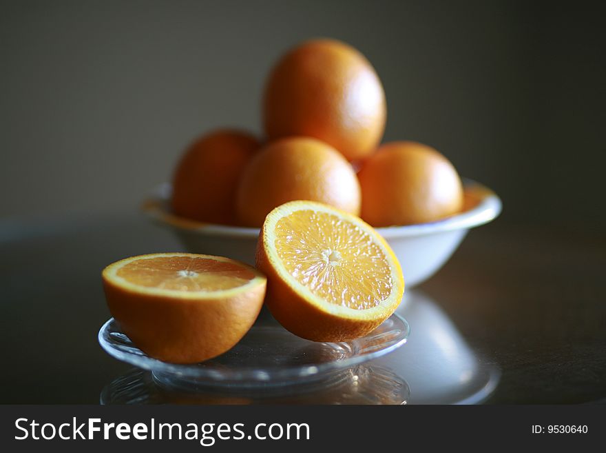 Sliced orange on a plate with bowl of oranges in background.