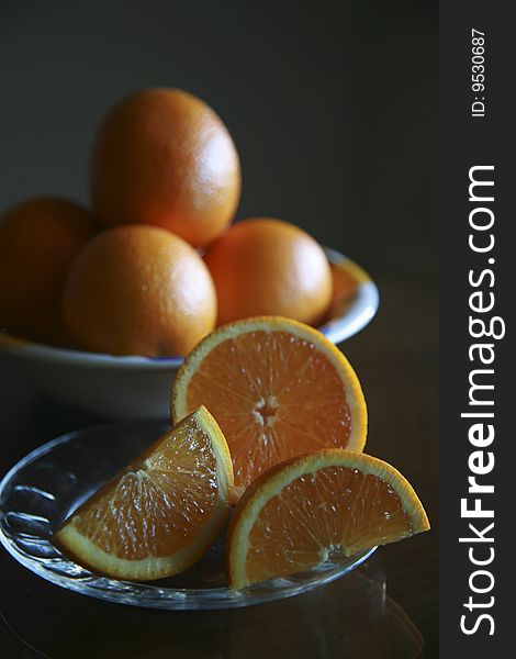 Sliced oranges on a plate with bowl of oranges in the background