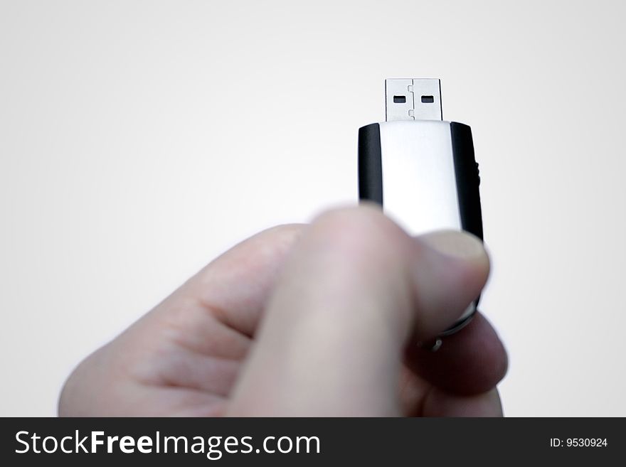 A hand holding a silver-black USB stick as if the person whould insert it into the computer, against a white gradient background. A hand holding a silver-black USB stick as if the person whould insert it into the computer, against a white gradient background