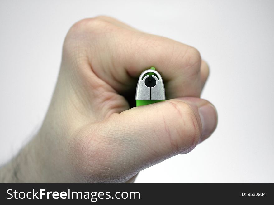 A hand/ fist holding a green and silver cigarette lighter, directing the gas nozzle towards the camera as in a top-down view, the hand pressing the trigger, against a white gradient background. A hand/ fist holding a green and silver cigarette lighter, directing the gas nozzle towards the camera as in a top-down view, the hand pressing the trigger, against a white gradient background