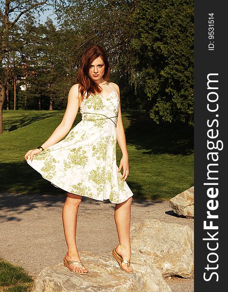 A pretty young girl standing on an rock in the park, with long red hair holding her dress and shooing her nice legs. A pretty young girl standing on an rock in the park, with long red hair holding her dress and shooing her nice legs.